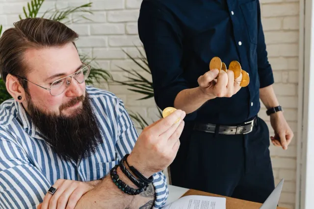 Imajen ida hatudu ema negósiu sira tuur hamutuk iha meja, ho komputador no dokumentu, hodi diskute estratéjia investimentu ba