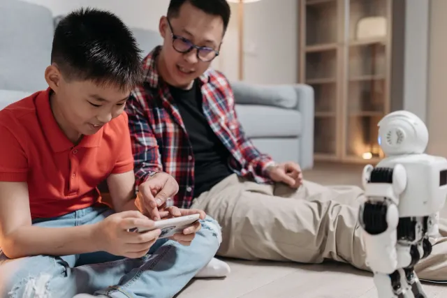 Imajen ida hatudu inan-aman ida ho labarik sira uza smartphone, ho ikon teknolojia kontrolu parental iha ekrã, hanesan simbol
