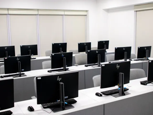 Imajen ida ne'e hatudu sala aula eskola negósiu ho estudante sira uza komputador no teknolojia AI ba dezempeñu negósiu