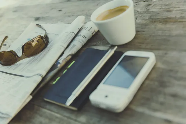Ema ida lee notísia iha smartphone ho kafé iha meza, hanesan ilustrasaun ba oinsá ita konsume notísia iha tempu agora