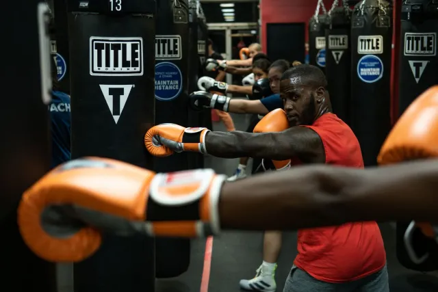 Floyd Mayweather Jr. hamriik iha ringue ho luvas boxe, nia rosto seriu, iha fundu luz neon, hatudu luta exhibition kansela ta