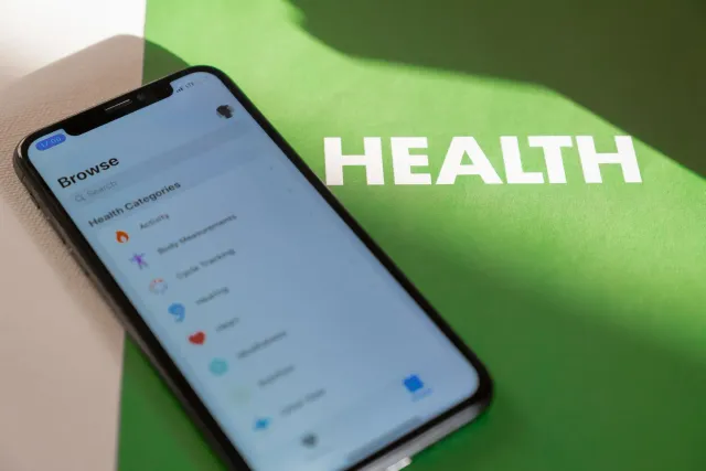 Ema ida uza smartphone ho aplikasaun saúde iha liman, iha futar alérjia no garrafa alkoól iha mesa, ho avizu risku kanser