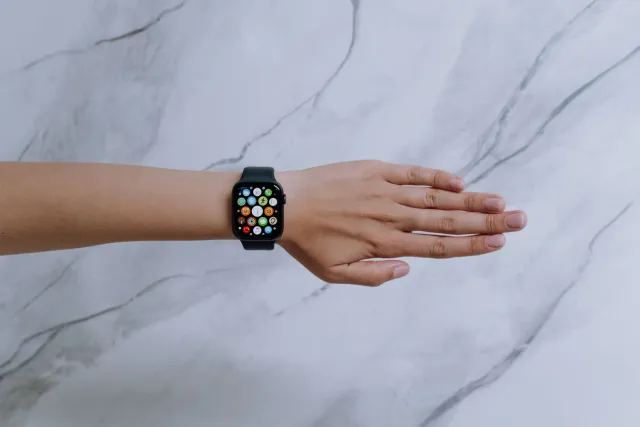 Imajen ida hatudu Apple Watch iha liman ema nian, ho ekrán hatudu gráfiku saúde no AI ikon, hanesan símbolu ba futuru monitor