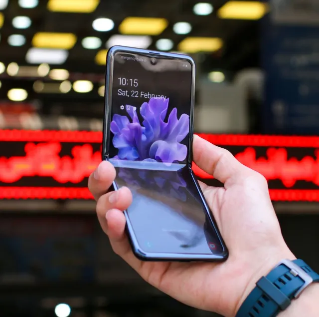 Ema uza Samsung Galaxy Z Fold 8 ho ekrã dobra, hatudu teknolojia foun iha ambiente servisu. Iha meja, dokumentu no kafé, simb