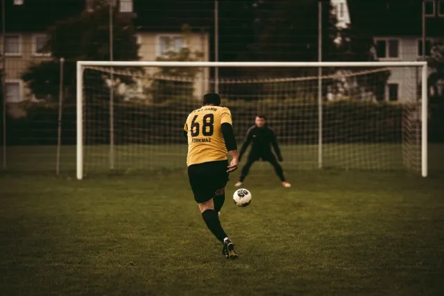 Jogador xuta penalty iha Mundiál Futebol 2026 ho goleiru prontu atu defende, iha estádiu cheia ho ema