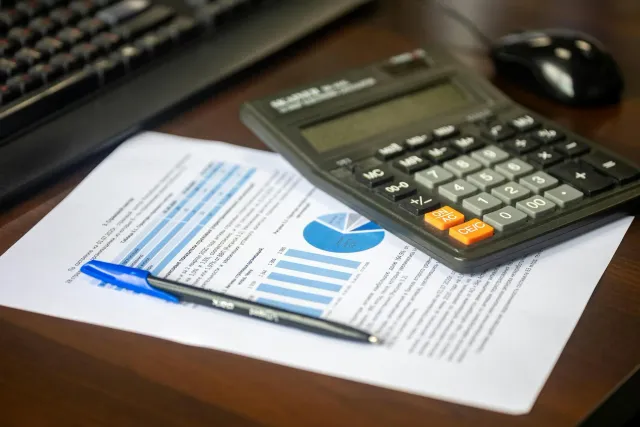 Imajen ida hatudu dokumentu finanseiru, kalkuladora, no lapis iha meja, hanesan símbulu ba planeamentu finanseiru ne'ebé mate