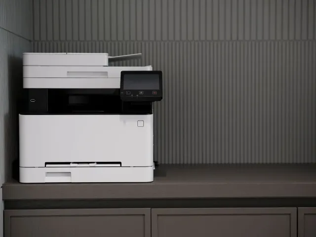Imajen ida hatudu printer foun SHARP iha ambiente eskritóriu modernu, ho komputadór no dokumentu sira