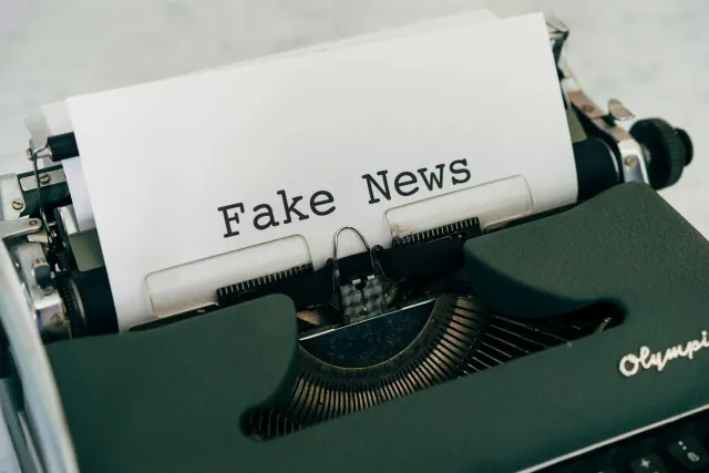 Imajen ida ne’ebé hatudu jornalista sira serbisu iha sala notisia ho tensaun, no iha fundu hatudu telemóvel ho mensajen falsu
