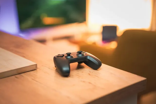 Imajen ida hatudu konsola Nintendo Switch 2 ho kontrolador iha mesa, ho jogu Star Fox iha tela, no kafé ida iha sorin, ilumin