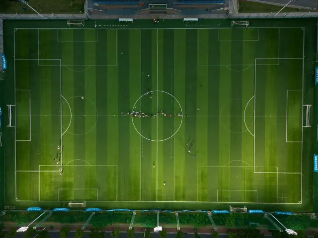 Imajen ida ne'ebé hatudu kontraste entre estadiu futebol boot no eskritóriu korporativu iha sidade, ho helikopteru iha roof n
