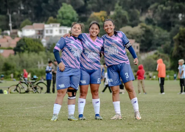 Imajen ida ne'ebé hatudu jogadoras kriket feto iha Women's T20 World Cup 2026, no iha fundu bandeira Kolombia no Gana, ho sim