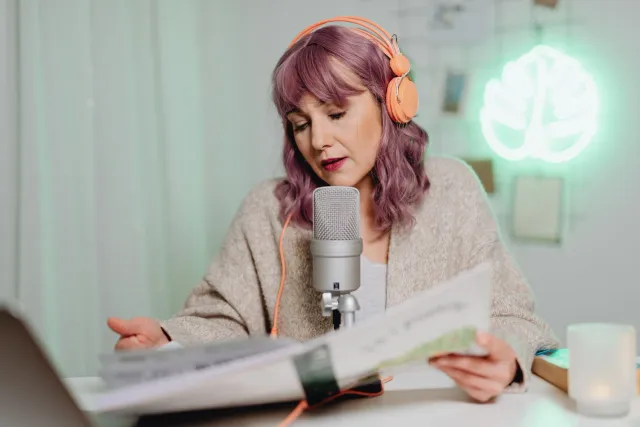 Feto ida koalia iha mikrofonu ba podcast kona-ba menopauza, ho sorriso no aparénsia forte, iha fundu ne'ebé relaxa hela.